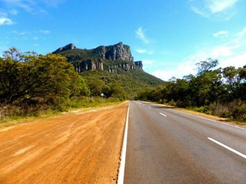 On the inter-urban road shown in the image, is it permissible to pull over or park on the passable unpaved hard…